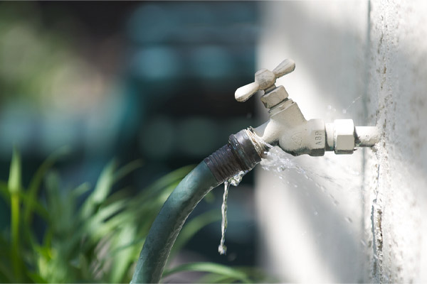 A water spigot with a green hose springs a leak