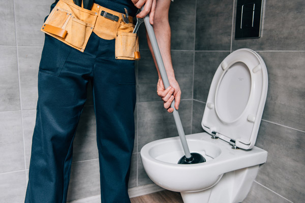 plumber unclogging toilet after homeowner flushed wipe