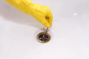 homeowner wearing yellow gloves removing hair from the sink drain