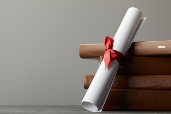 brown books and rolled certificate depicting plumbing license and certificate