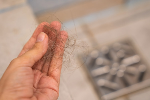 image of a homeowner holding hair from clogged shower drain
