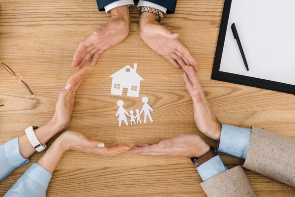 people making circle with hands surrounding a cutout house and family depicting home protection