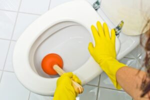 homeowner using an orange plunger in a clogged toilet