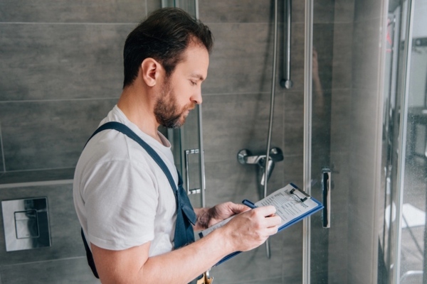 Side view of male plumber making notes in clipboard in a modern bathroom